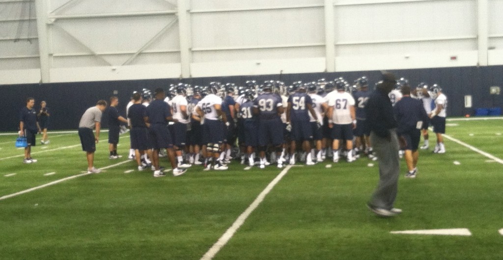 UConn football team huddles around Coach Bob Diaco at first practice of season Saturday. (Ken Davis photo)